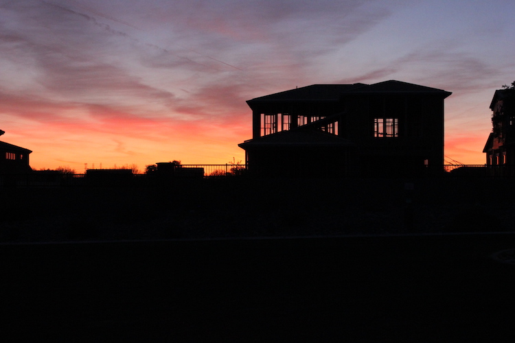 A house under construction in silhouette against an Arizona sunset